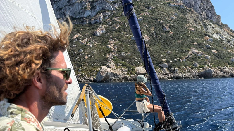 Personas contemplando la puesta de sol frente al peñón de Es Vedrà desde un velero